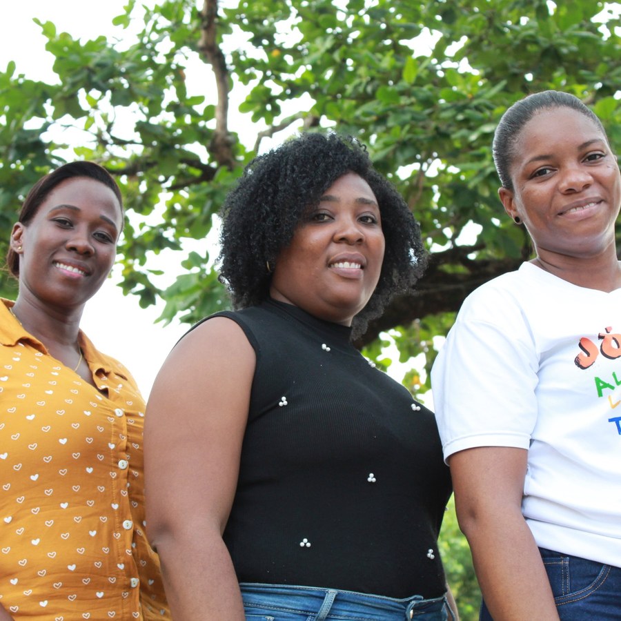Mujeres de Oro — tres mujeres sonríen a la cámara frente a un árbol