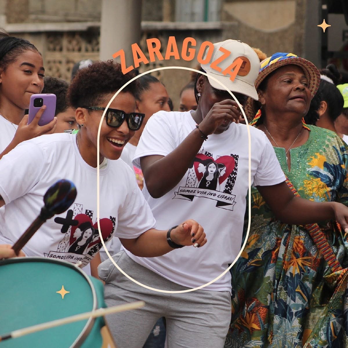 Fotografía de una marcha en Zaragoza: varias personas con camisetas blancas «Somos vida, ¡no cifras!», una con gafas de sol sonriendo y un tambor en primer plano, con el nombre «Zaragoza» en naranja y un marco de arco.