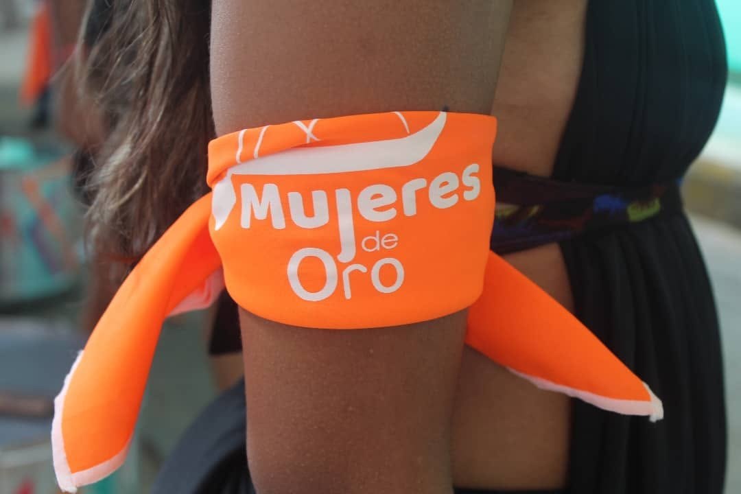 Primer plano de un pañuelo naranja con el logo de Mujeres de Oro atado en el brazo de una persona.