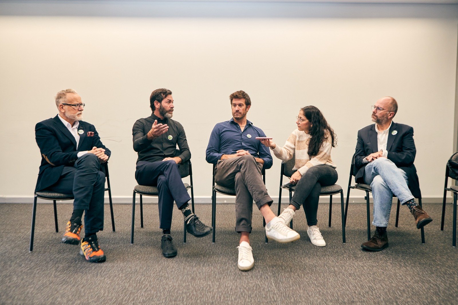 Fotografía de cinco participantes sentados en sillas frente a una pared clara, conversando durante el panel.